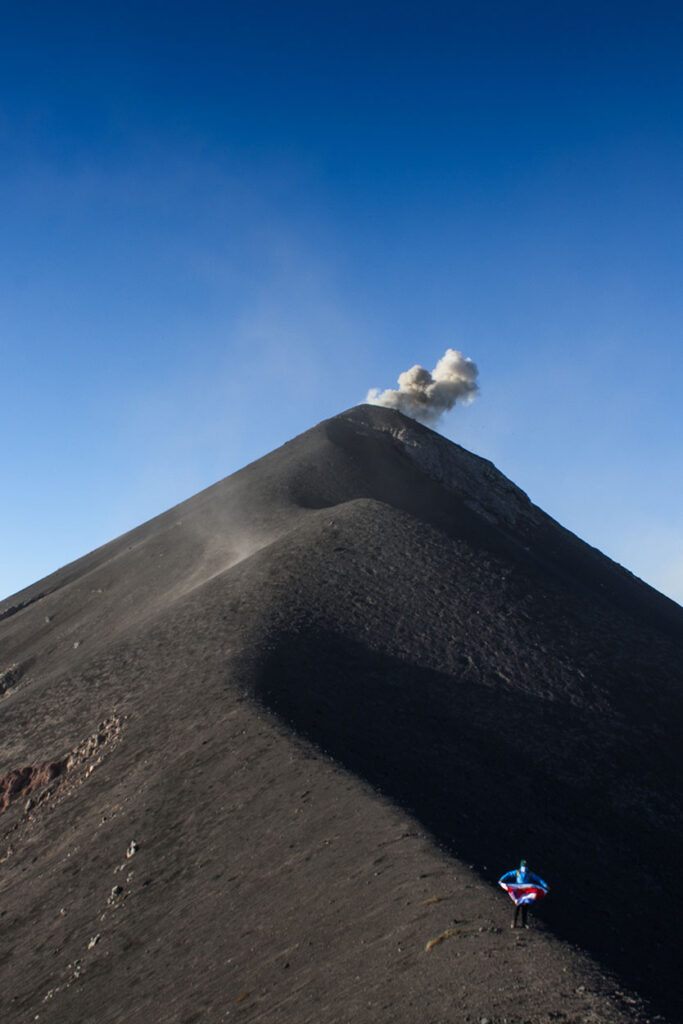 Senderista posando con la bandera de Costa Rica en el camellón del Volcán de Fuego, Guatemala