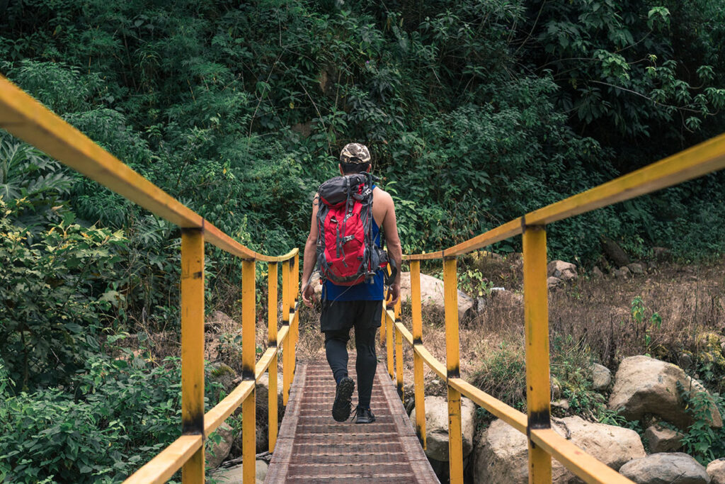 excursionista cruza un puente con una mochila roja, rodeado de arbustos y árboles verdes en la selva tropical del cerro Ena, Costa Rica.